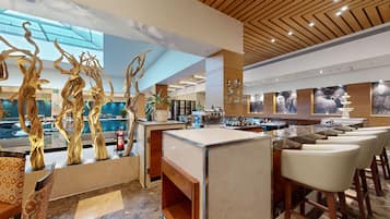 Un espace bar moderne doté d’un comptoir en marbre, de tabourets de bar et de sculptures en bois décoratives.