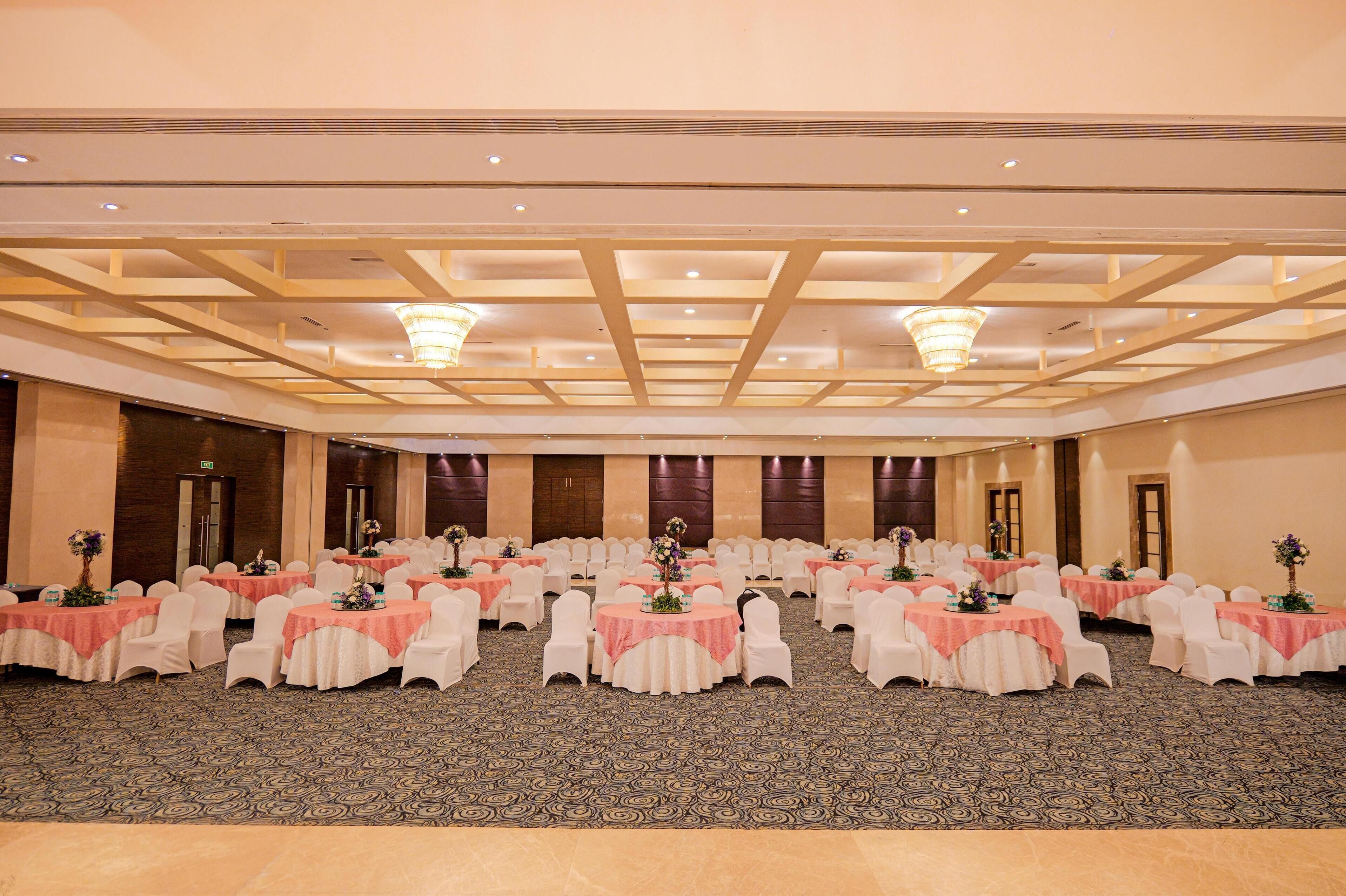 A large conference room with tables set for a meeting, featuring a patterned carpet and a high ceiling with exposed beams.