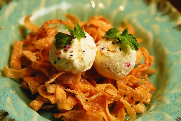 Two scoops of ice cream on a bed of orange-colored, crispy snacks, garnished with mint leaves.