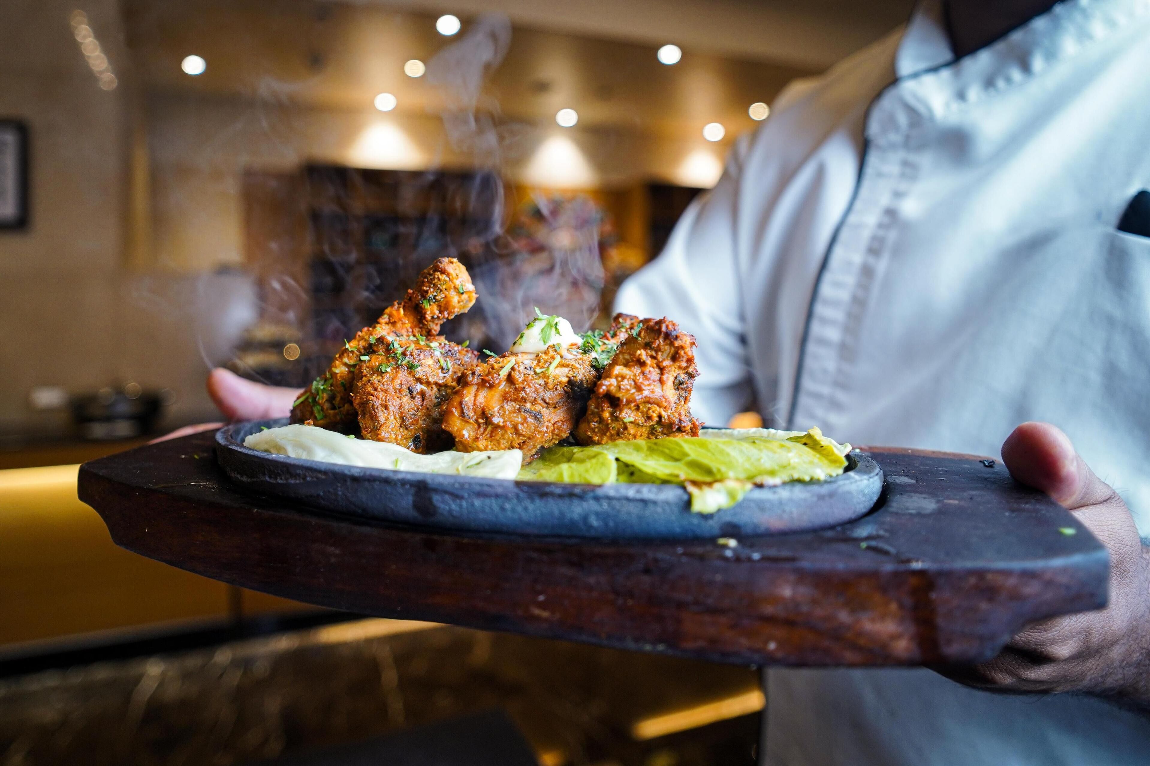 A chef holding a plate of food with a side of sauce and greens.