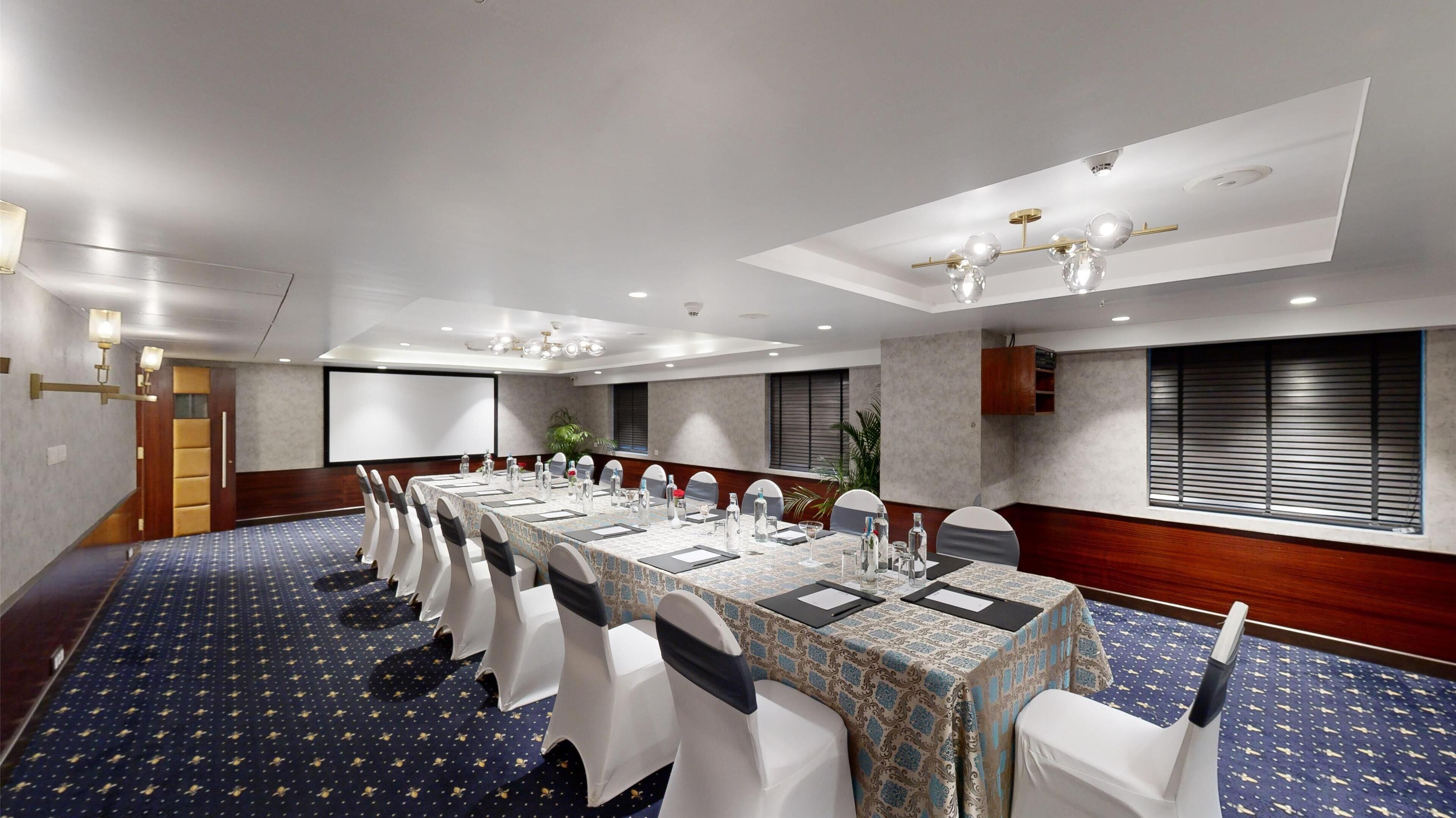 A conference room with a long table, white chairs, and a projector screen.
