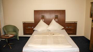 A hotel room with a large bed, two pillows, a small round table, and a green armchair.