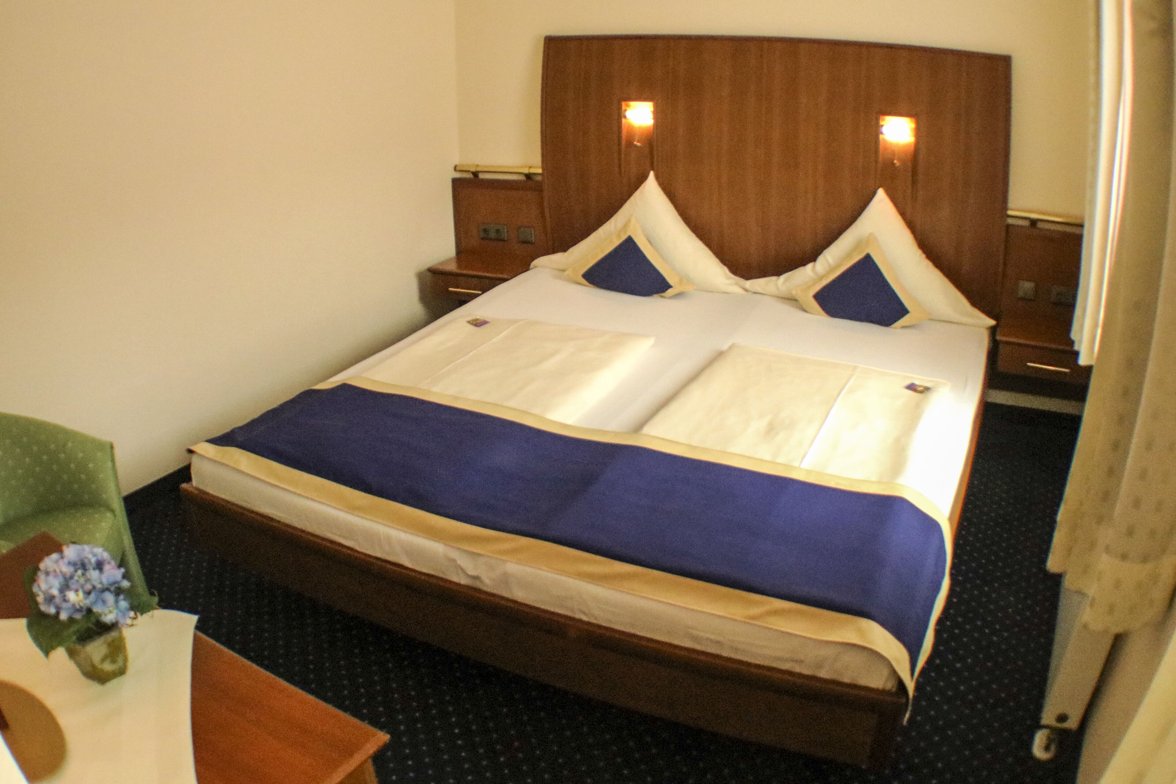 A hotel room with a large bed, wooden headboard, two bedside tables, and a green armchair.