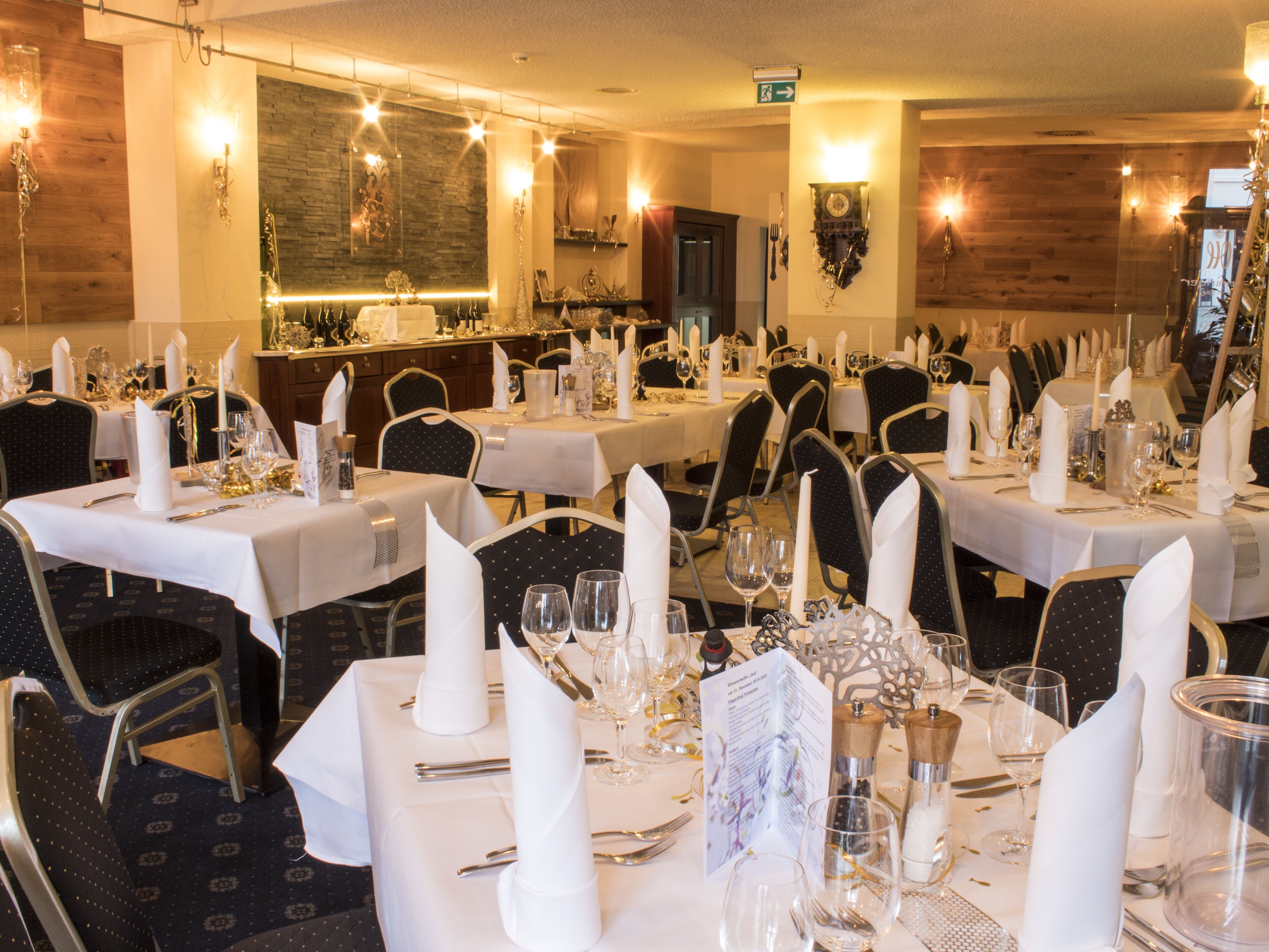 A restaurant with multiple tables set for dining, featuring white tablecloths, neatly arranged cutlery, and candles.