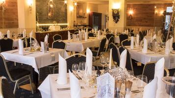 A restaurant with multiple tables set for dining, featuring white tablecloths, neatly arranged cutlery, and candles.