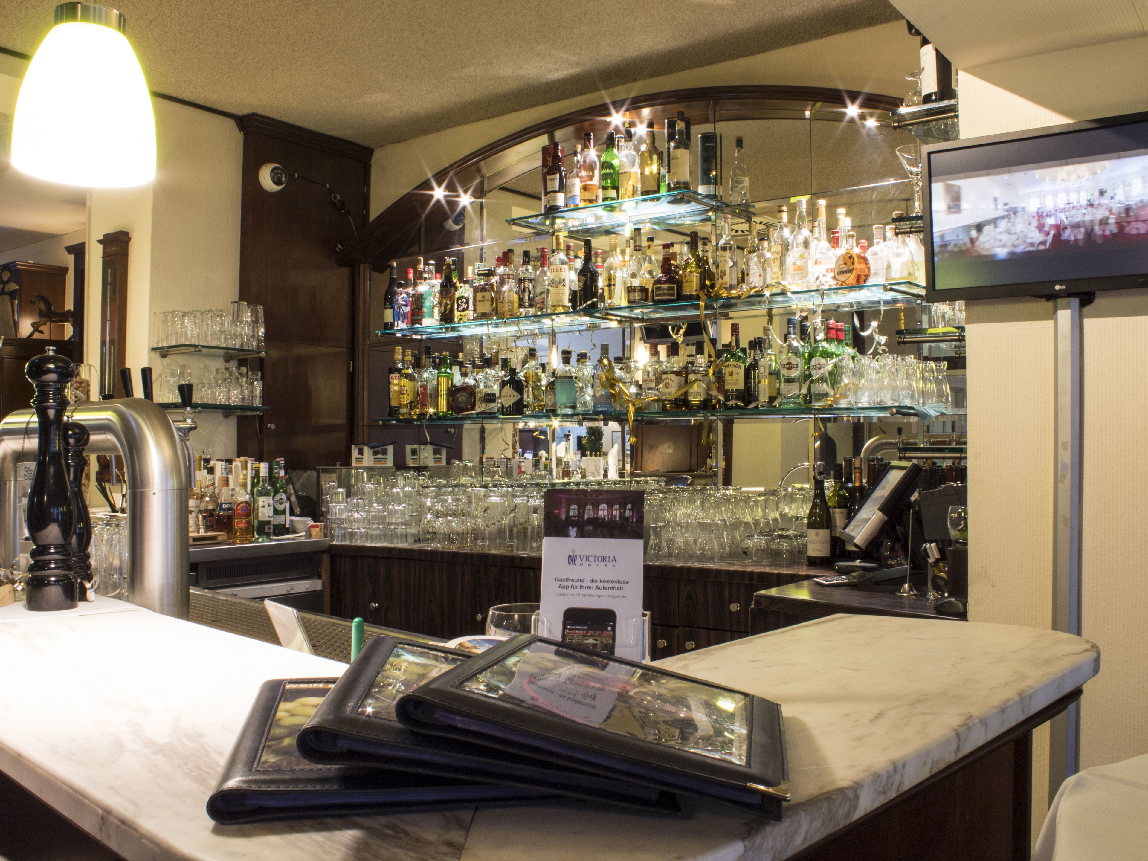 A bar area with multiple shelves of bottles and glasses, a cash register, and a menu stand.