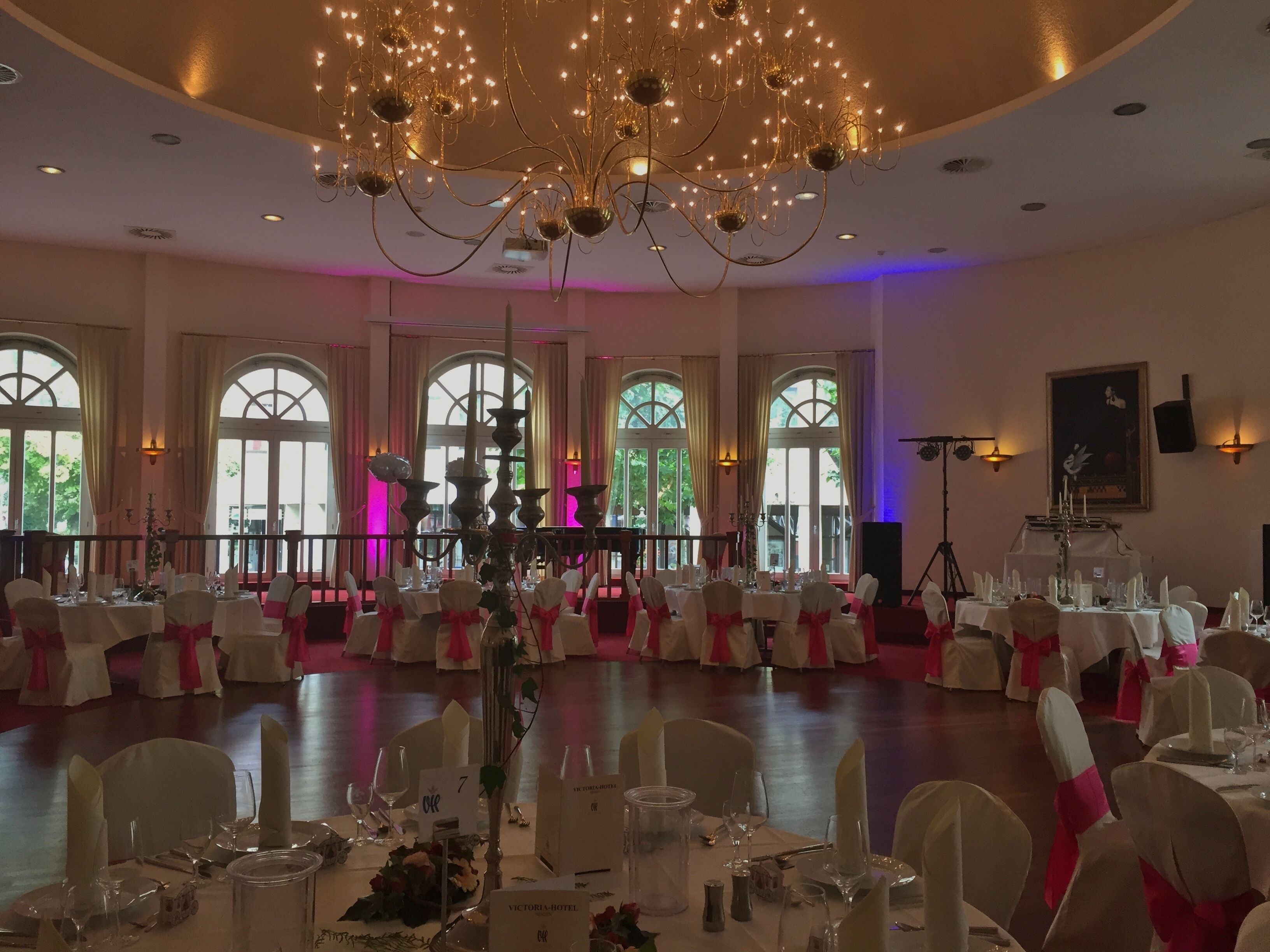 Un salón de banquetes con mesas redondas, sillas blancas y una araña.