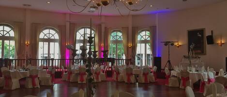 Un salón de banquetes con mesas redondas, sillas blancas y una araña.