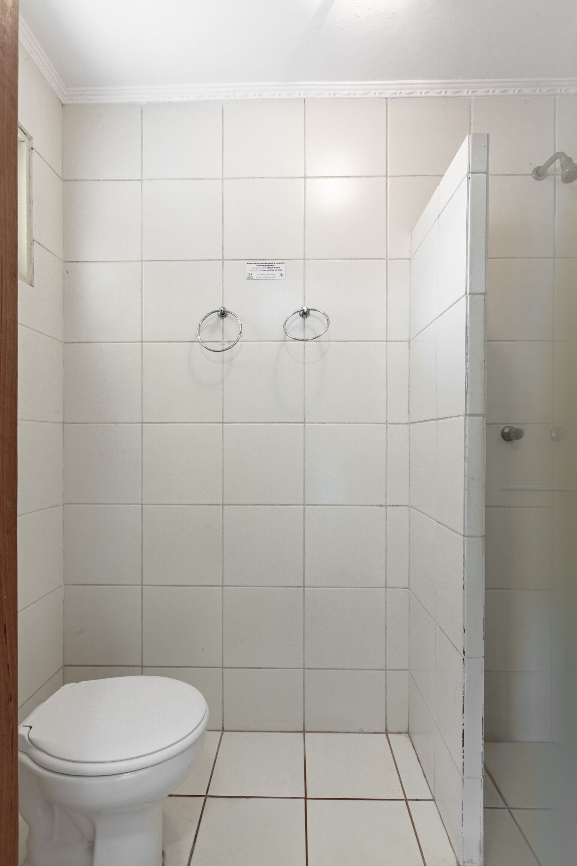 A bathroom with white tiles, a toilet, and a shower area.