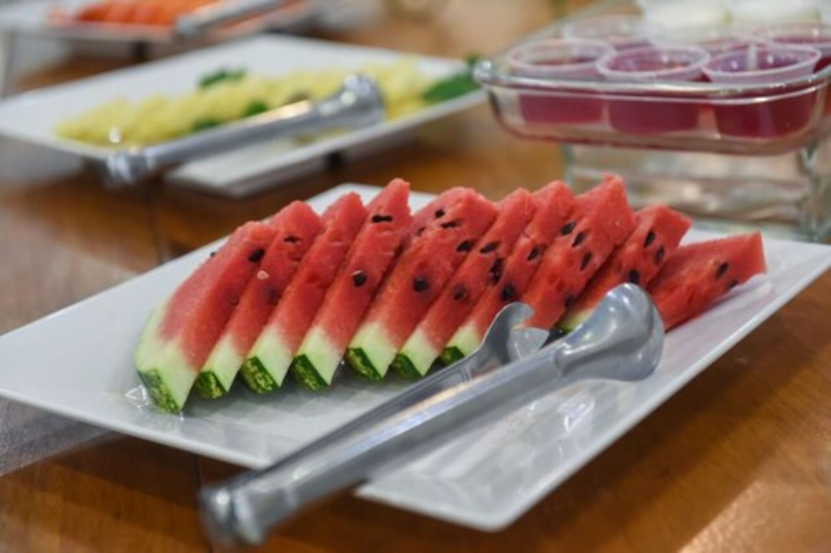 Une table de buffet proposant une variété de plats, notamment des tranches de pastèque et d’autres fruits.
