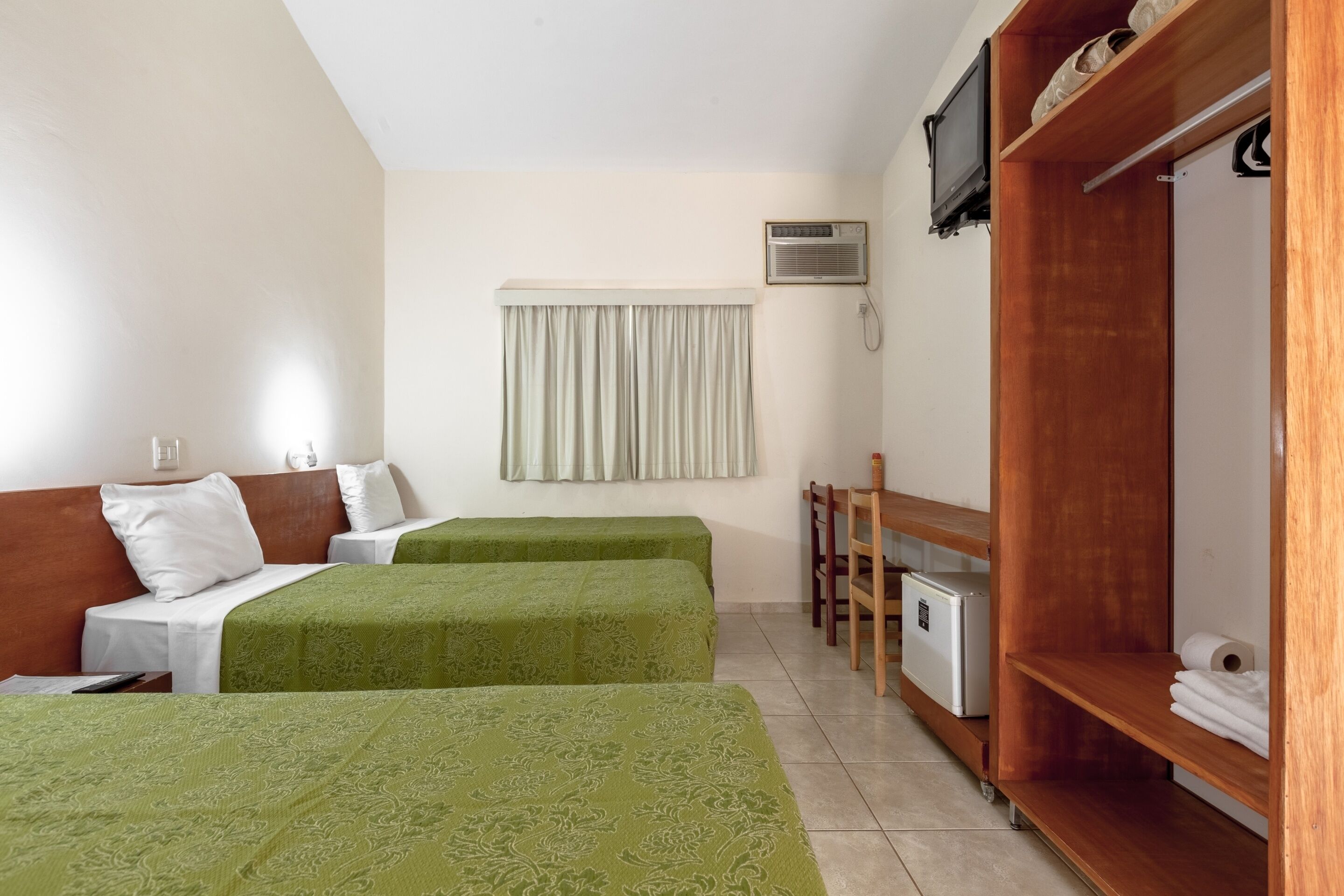 Habitación de hotel con dos camas, un escritorio, un armario y aire acondicionado.