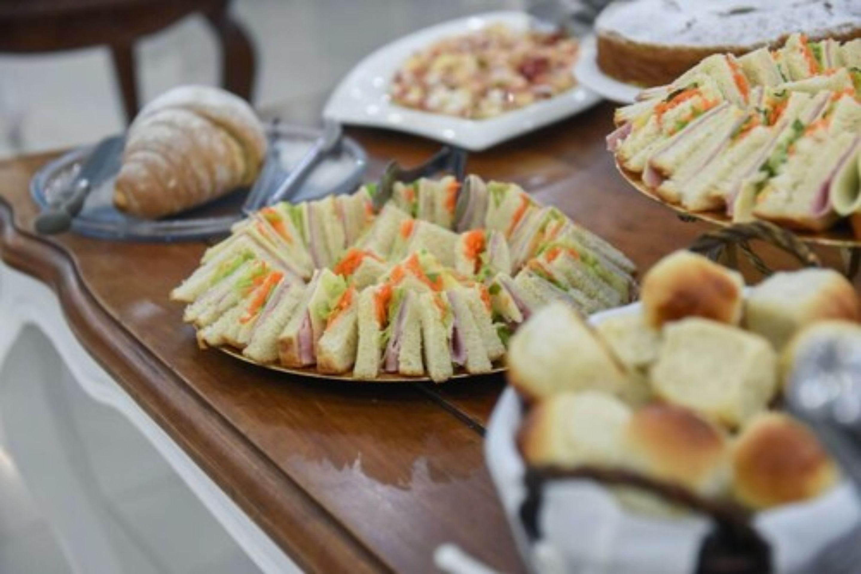 A buffet table with sandwiches, a croissant, and other pastries.
