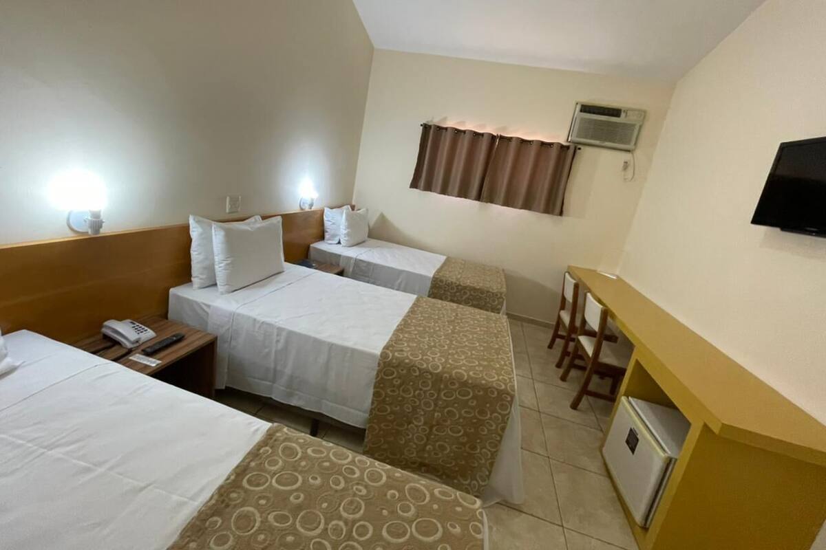 Une chambre d’hôtel avec deux lits simples, un bureau avec des chaises, une télévision et un appareil de climatisation.