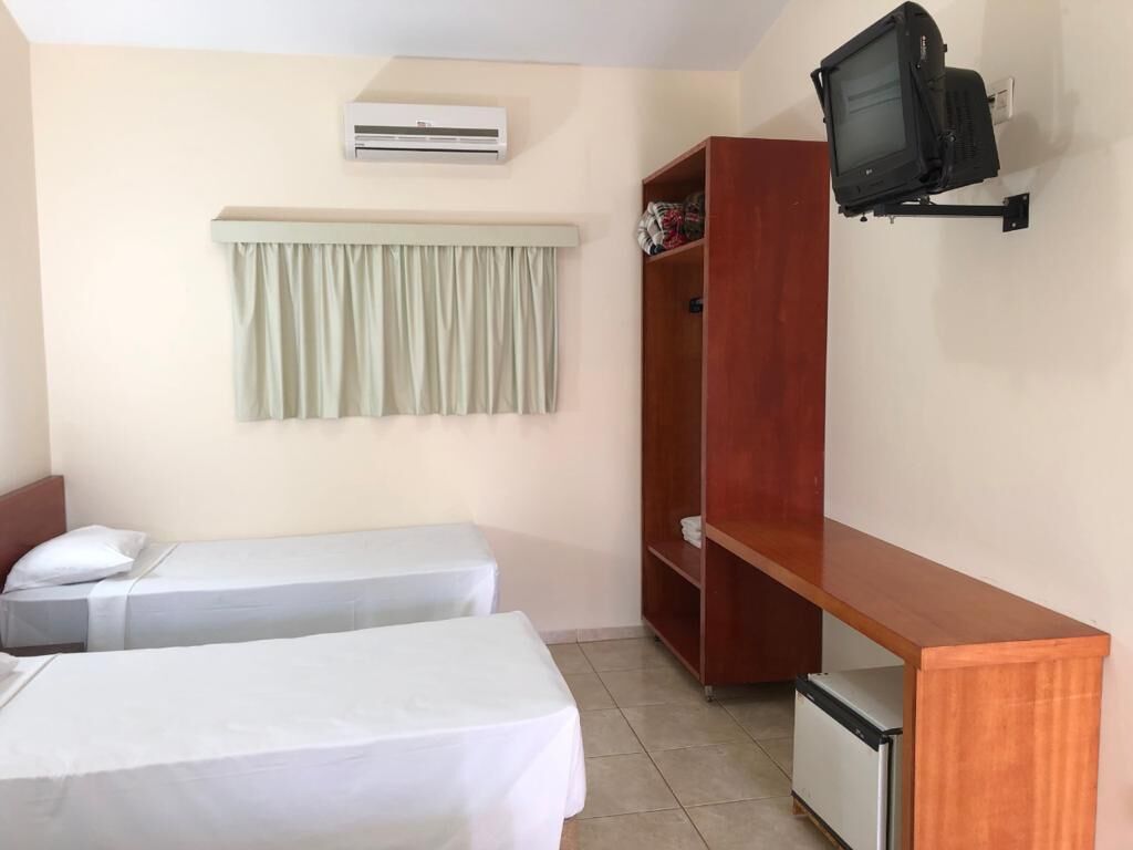 Quarto com duas camas, um guarda-roupa de madeira, uma televisão fixada na parede e um ar condicionado.