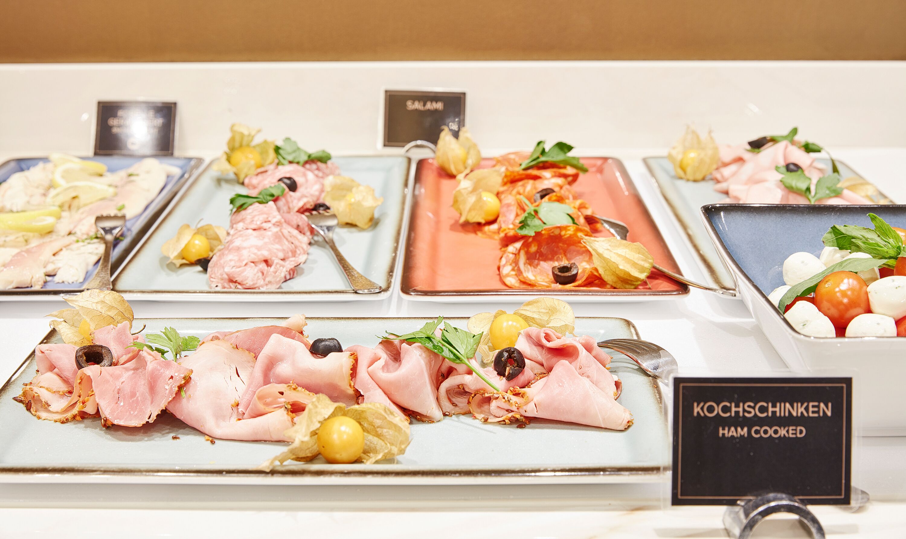 A buffet with various dishes including ham, olives, and vegetables.
