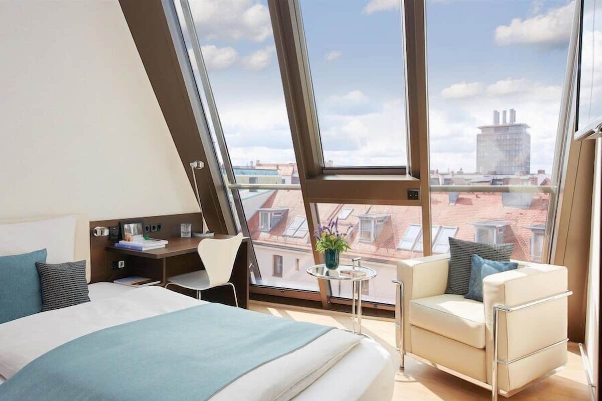 A modern bedroom with a large skylight, a bed, a small table, and a chair.