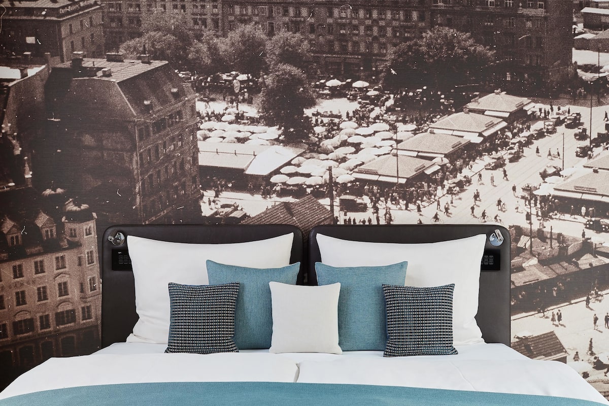 A bed with a cityscape mural on the wall behind it.