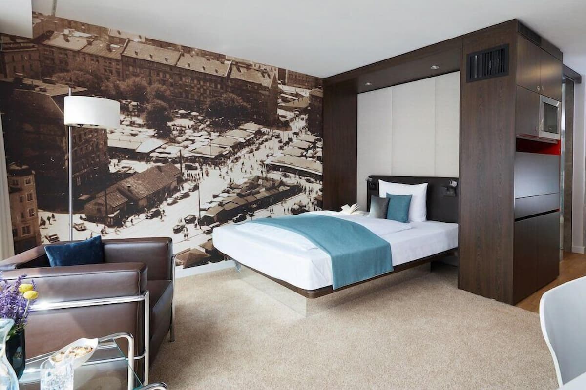 A modern hotel room with a bed, a desk, a chair, and a large window.