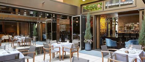 An outdoor dining area with tables and chairs, a bar, and a staircase leading to an upper level.
