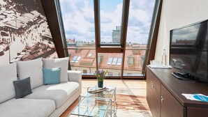 A modern living room with a sofa, a glass coffee table, a TV, and a view of the cityscape through large windows.