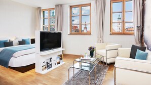 A modern hotel room with a bed, a flat-screen TV, a glass coffee table, and a sofa.