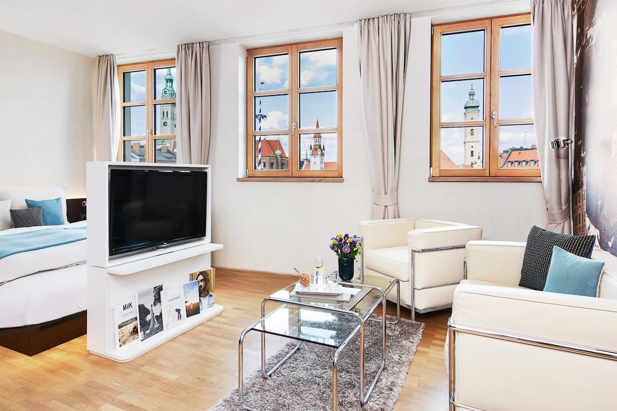 A modern hotel room with a bed, a flat-screen TV, a glass coffee table, and a sofa.