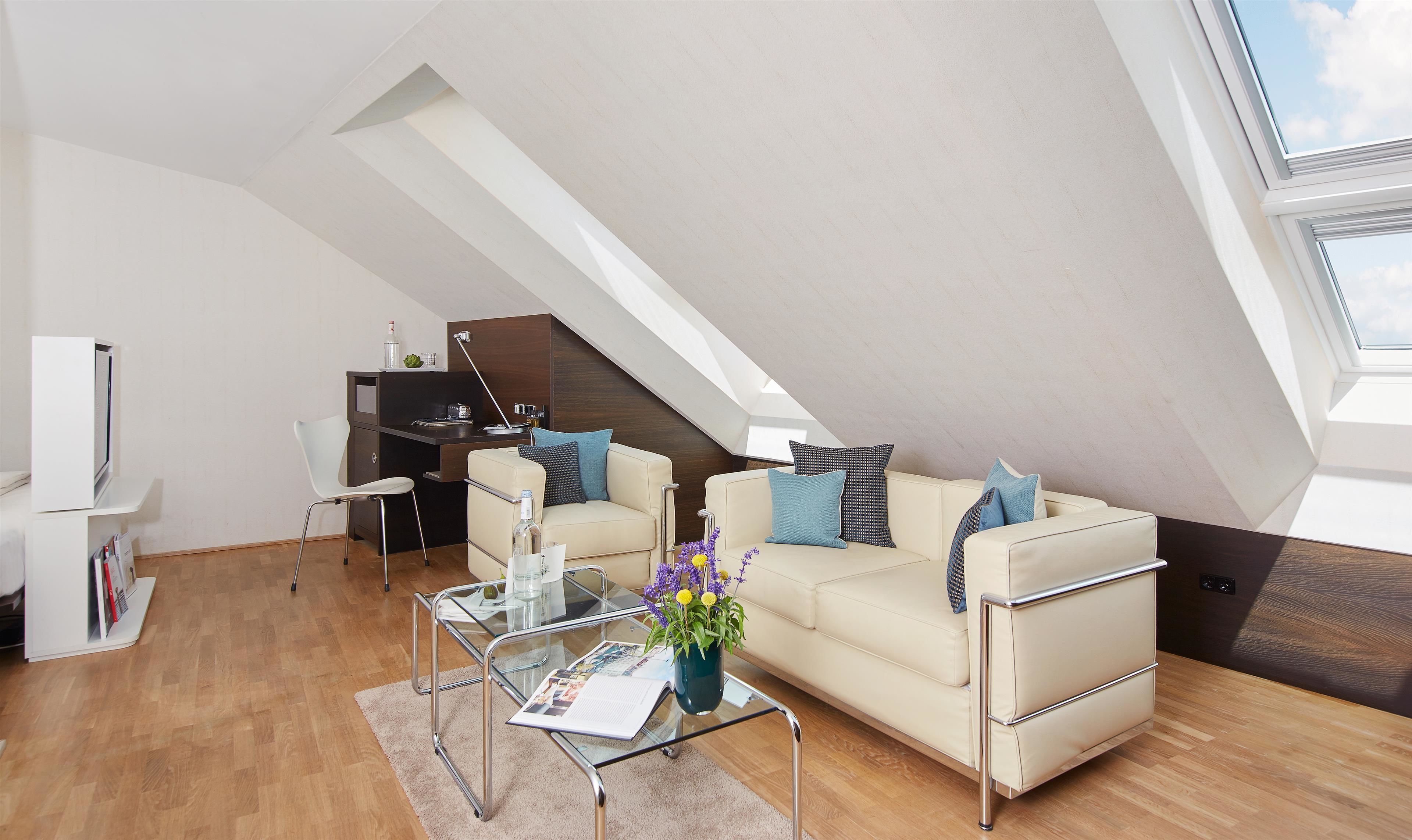 A modern loft apartment with a high ceiling, a glass coffee table, a beige sofa, and a small desk area.