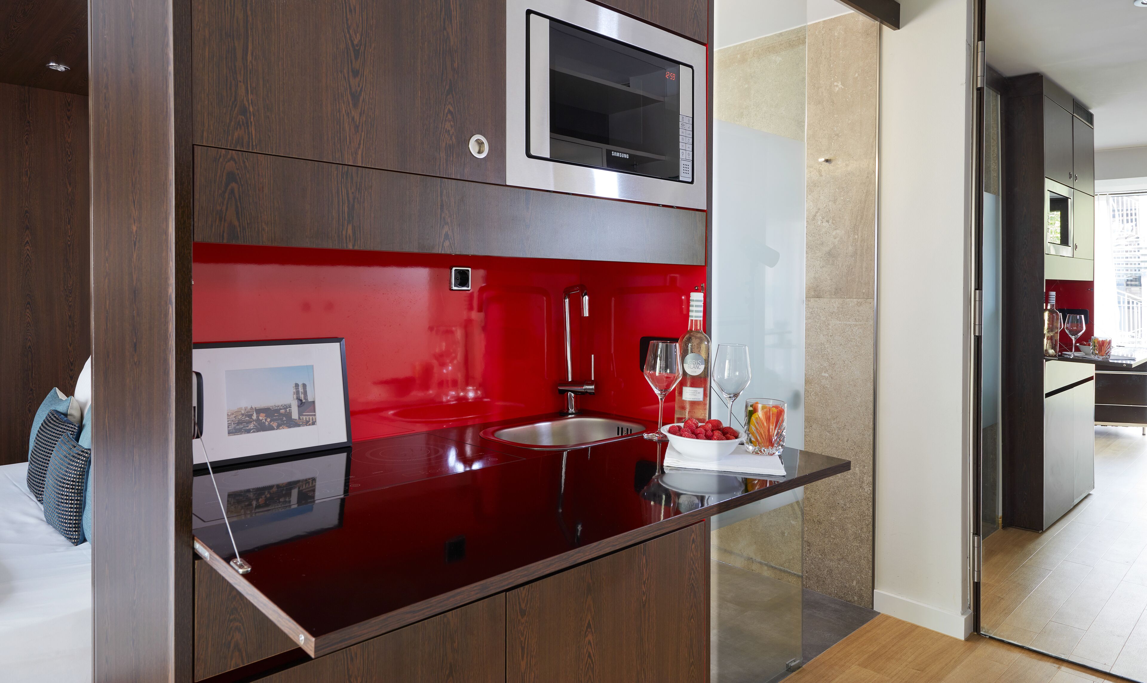 Una cocina moderna con microondas integrado, salpicadero rojo y un lavamanos de acero inoxidable.