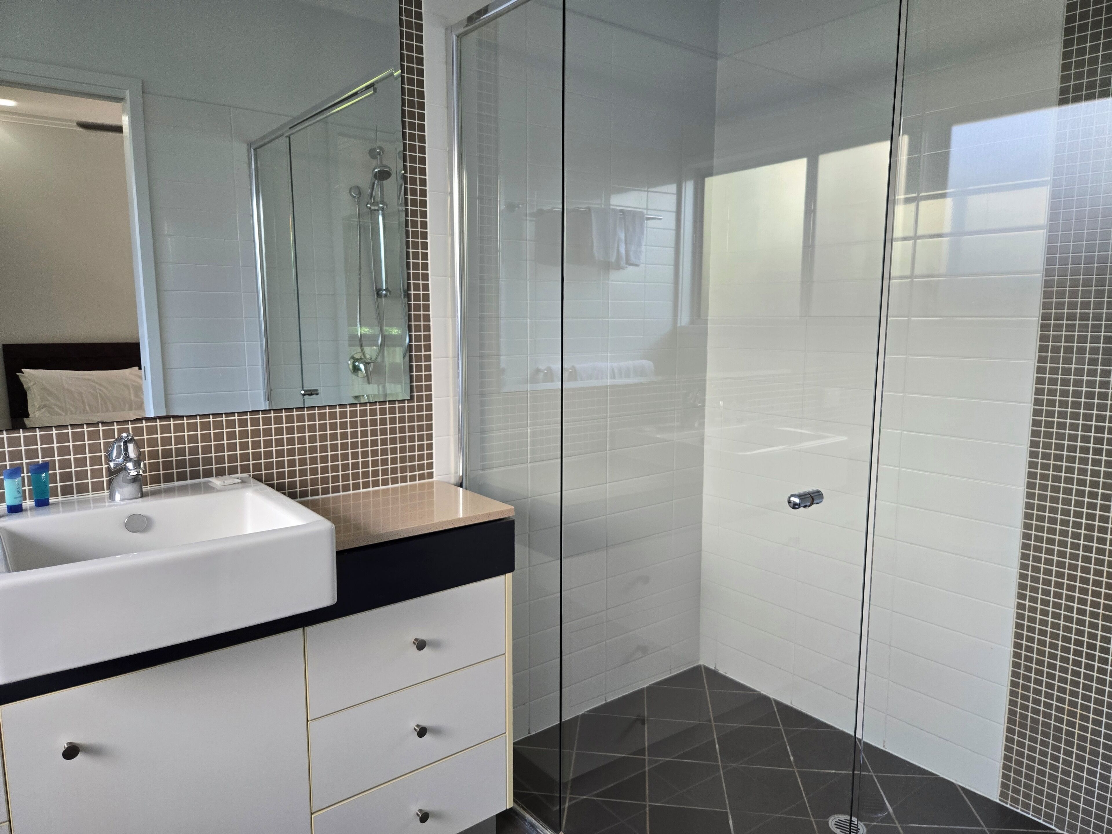 A modern bathroom with a glass shower enclosure, a white sink with a black countertop, and a mirror above the sink.