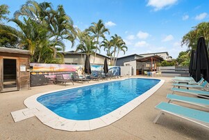 Una piscina con sillones de descanso, palmeras y un mural.