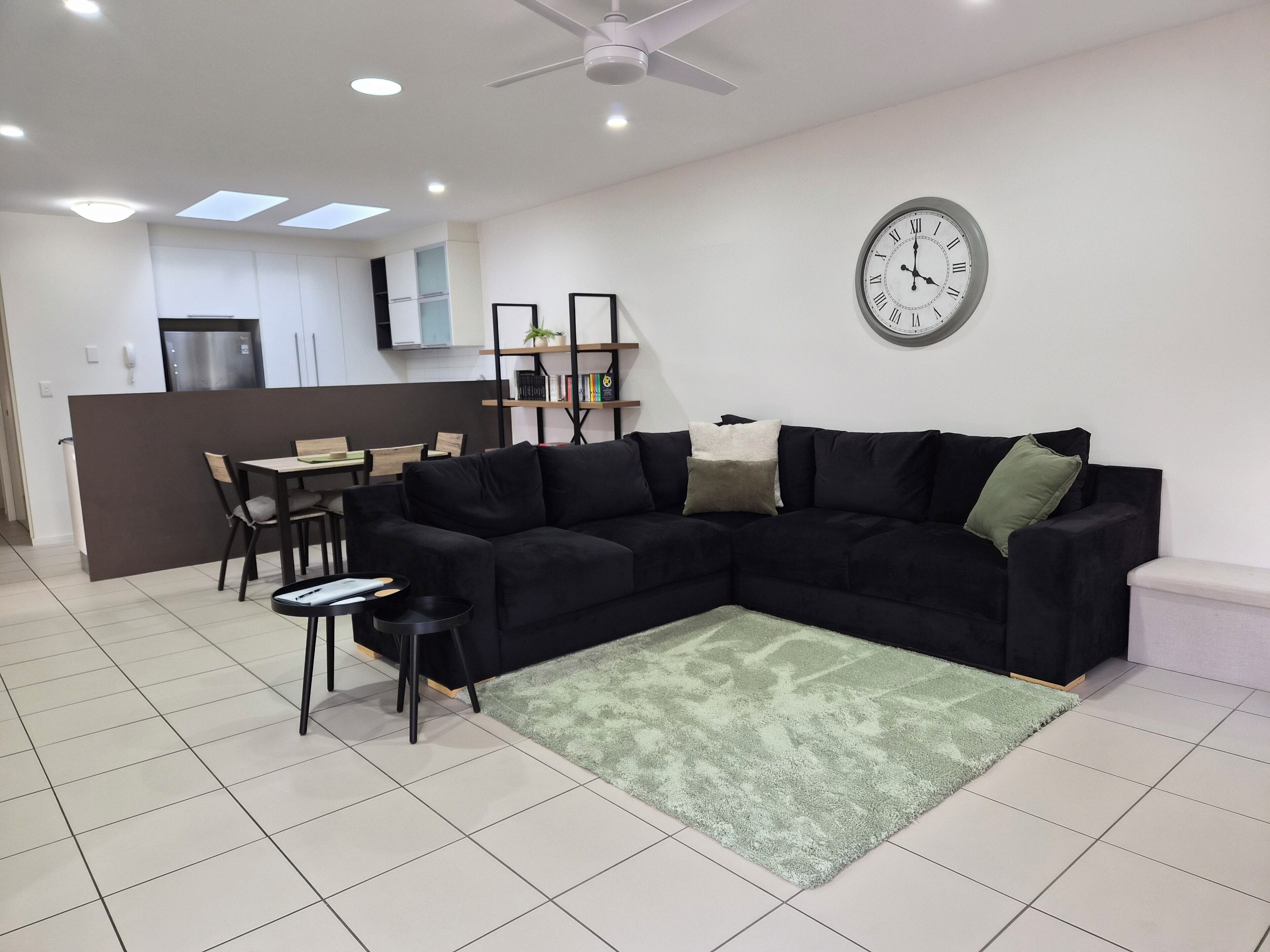 Un salon moderne avec un canapé d’angle, un coin repas et une cuisine en arrière-plan.