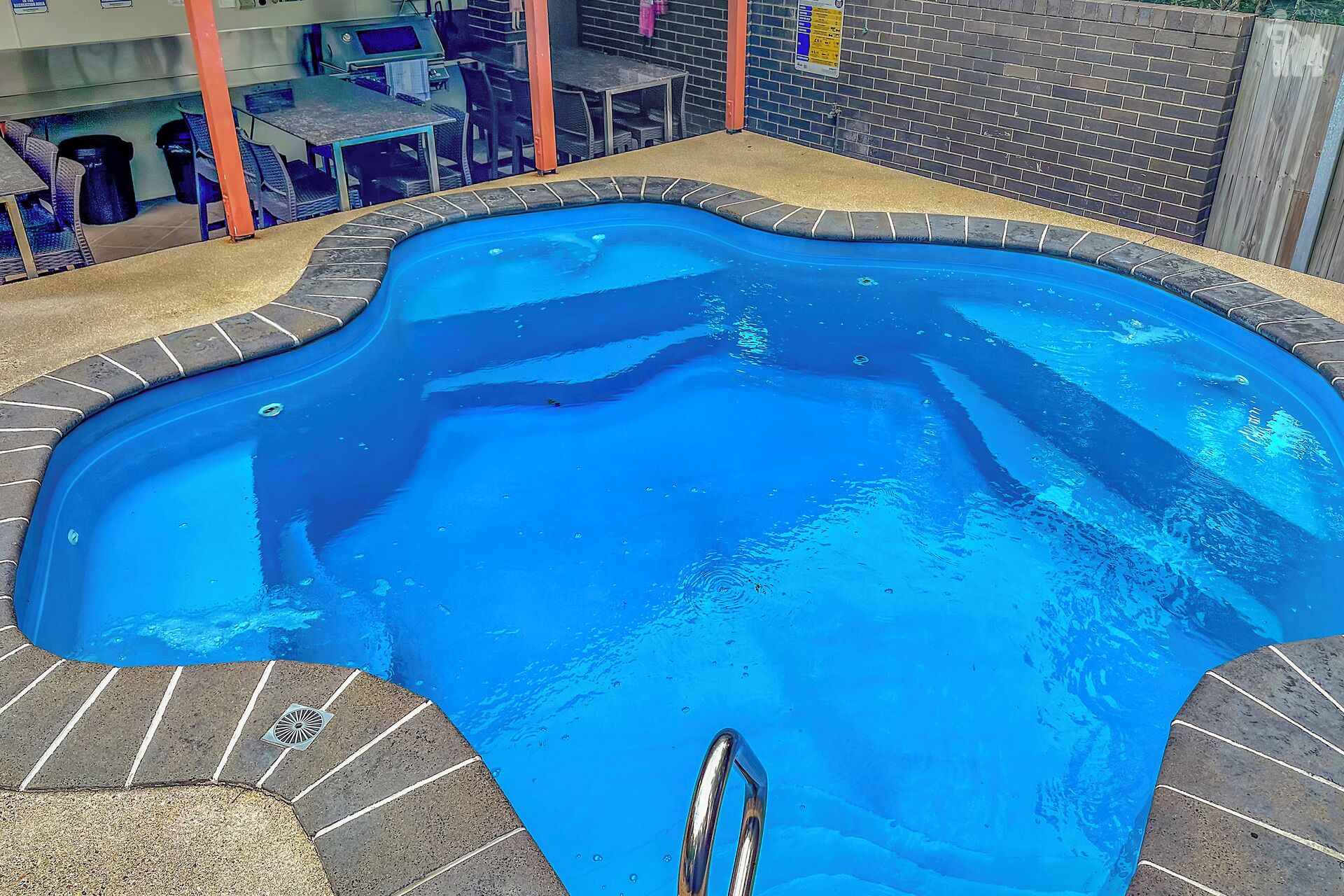 A swimming pool with a unique shape, surrounded by a brick border and a tiled deck.