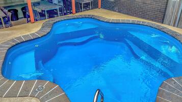 A swimming pool with a unique shape, surrounded by a brick border and a tiled deck.