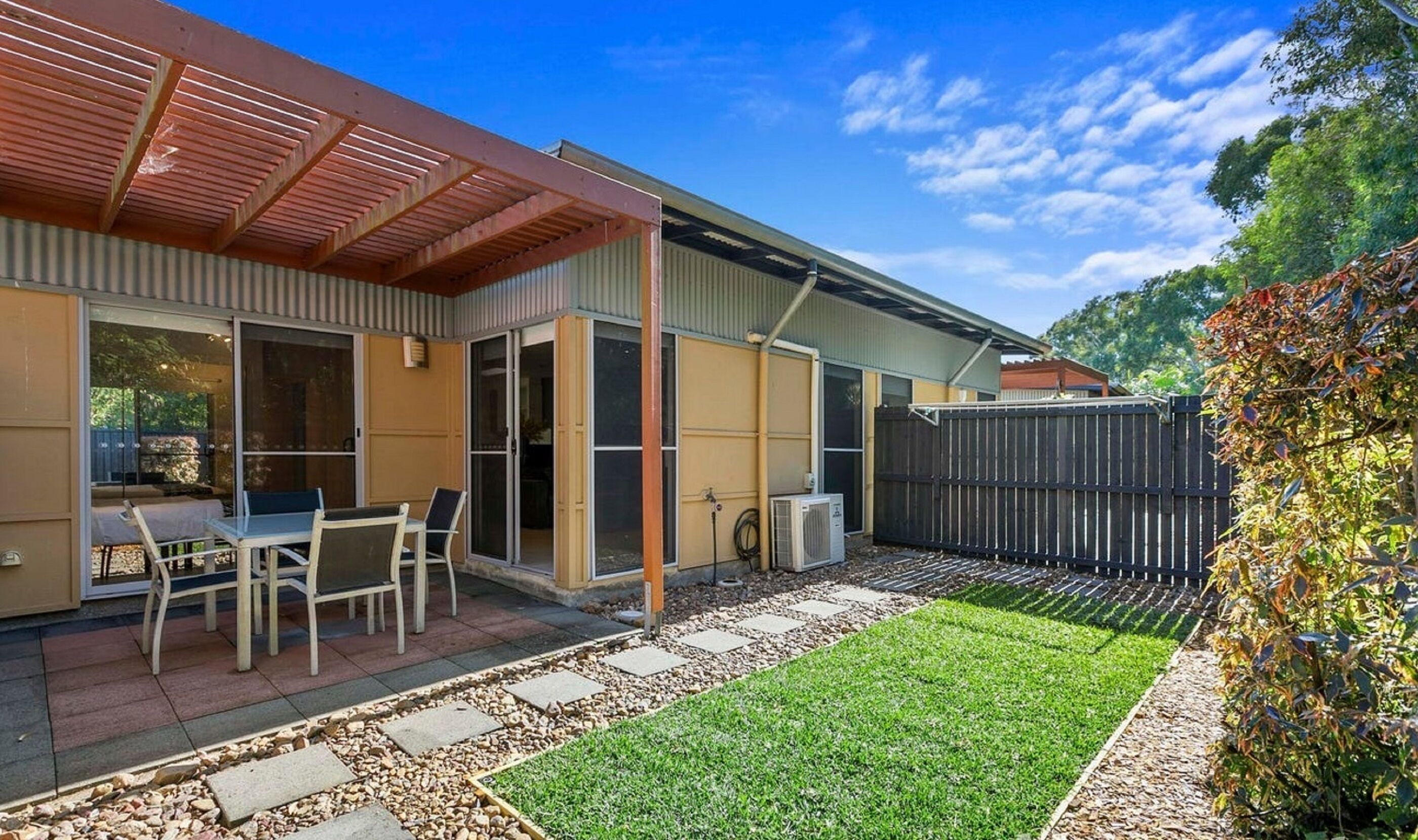 A residential backyard with a patio, a covered seating area, a lawn, and a wooden fence.
