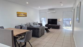 A modern living room with a sofa, TV, and dining area.