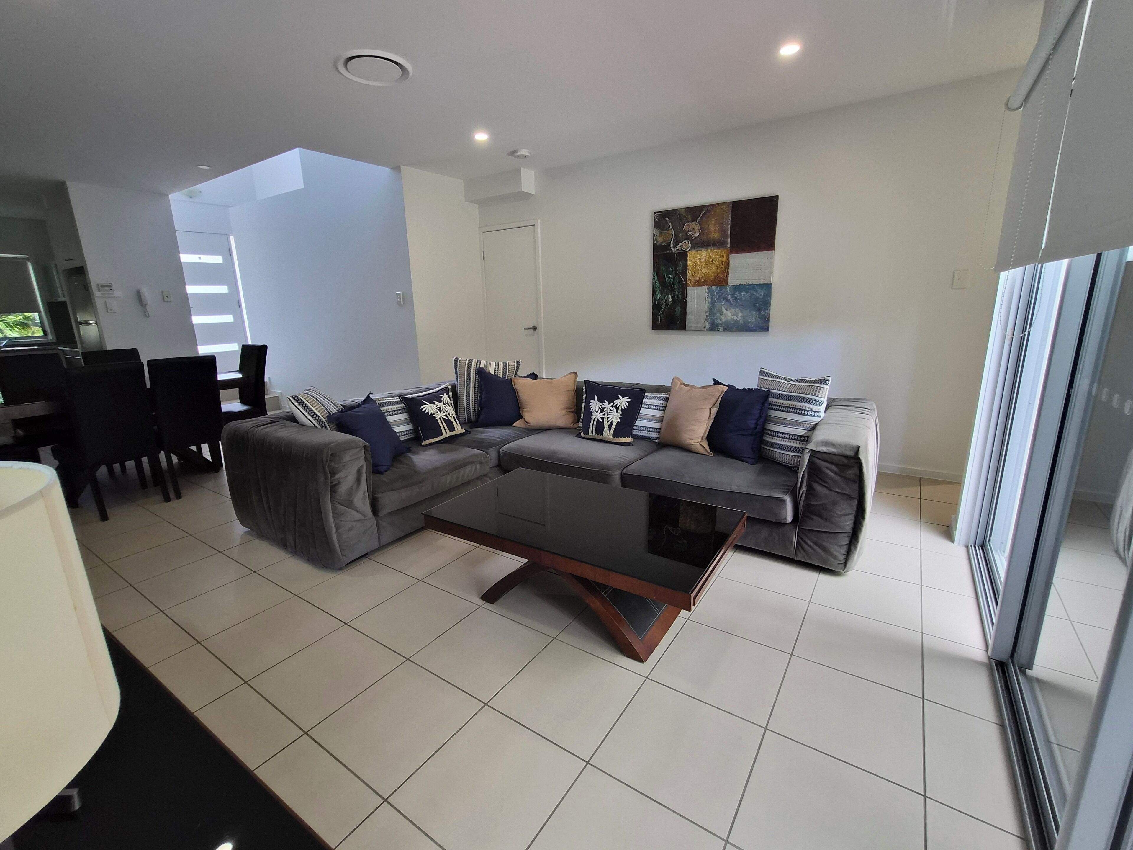 A modern living room with a grey sectional sofa, a glass coffee table, and a dining area with a table and chairs.