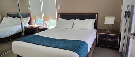 Habitación de hotel con una cama grande, dos mesitas de noche, un tocador, un espejo y una puerta.