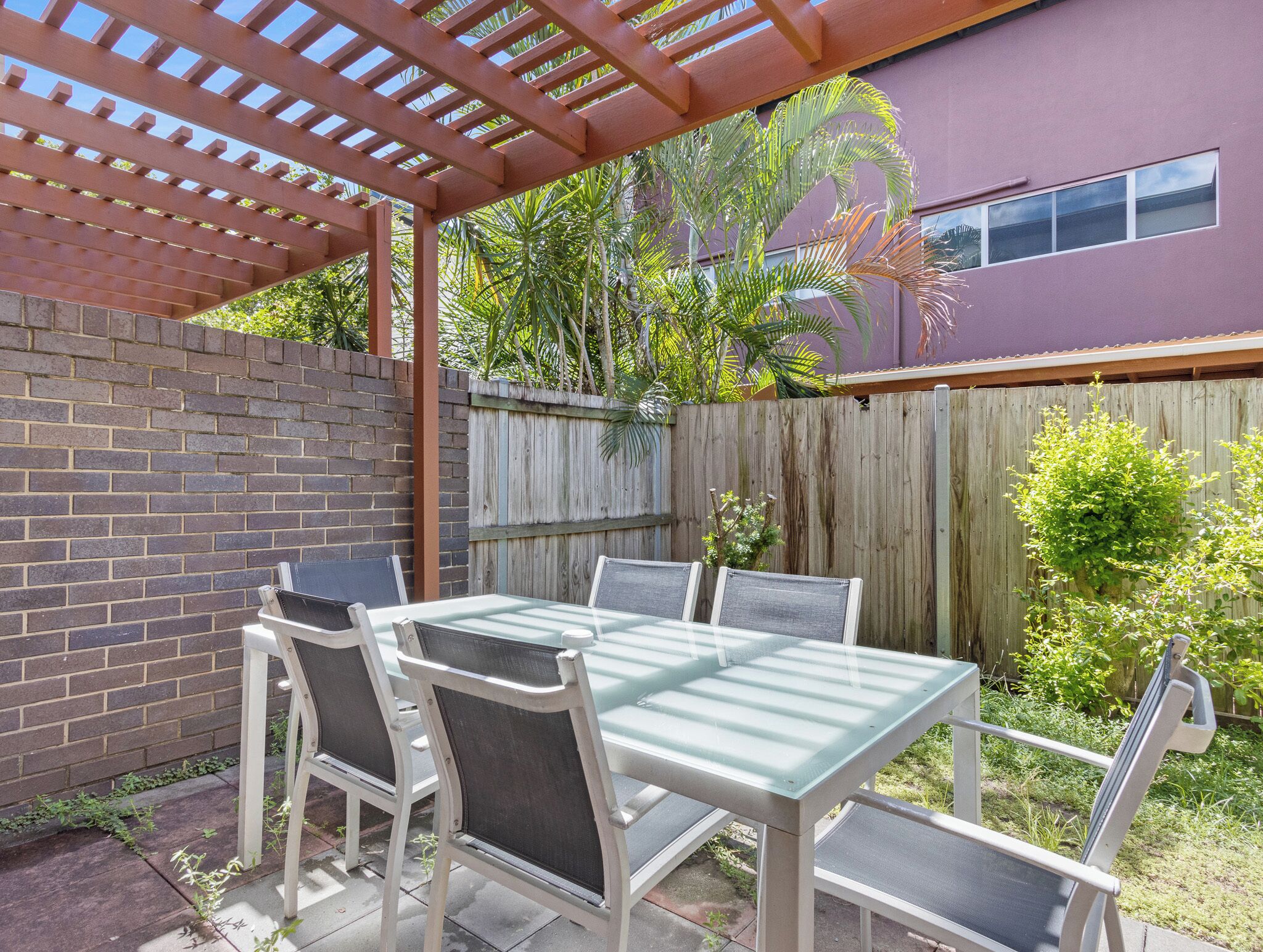 An outdoor patio with a table and chairs, a brick wall, and a wooden fence.