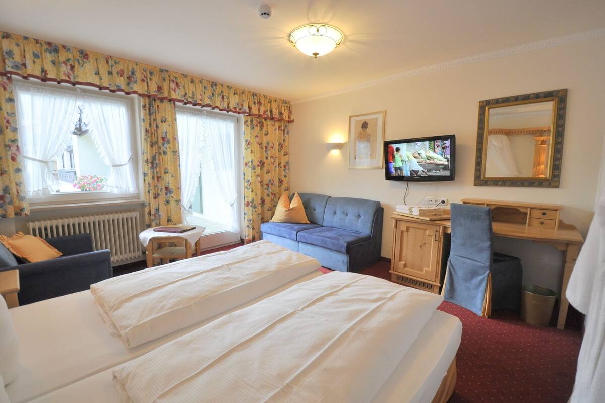 A hotel room with two beds, a desk, a television, and a window with curtains.