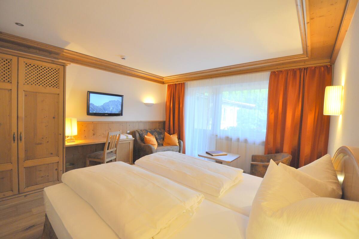 A hotel room with two beds, a desk, a chair, a television, and a window with curtains.