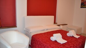 Una habitación de hotel con una colcha roja, cabecera blanca y una silla blanca.
