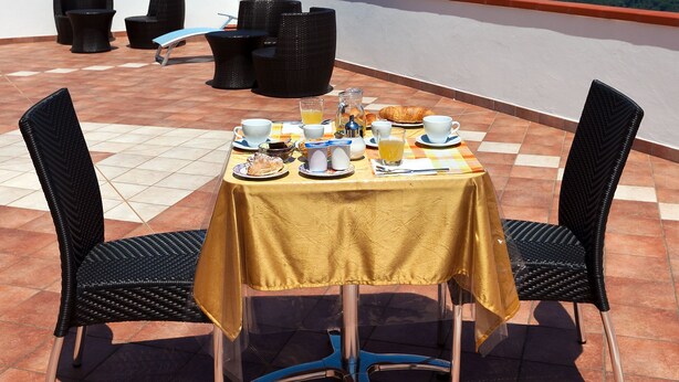 Una terraza con una mesa preparada para el desayuno, sillas y una vista panorámica del paisaje.