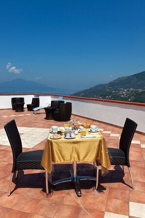 A terrace with a table set for breakfast, chairs, and a scenic view of the landscape.