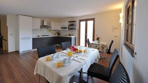 Un comedor con una mesa dispuesta para dos personas, una cocina al fondo y una puerta que da a otra habitación.