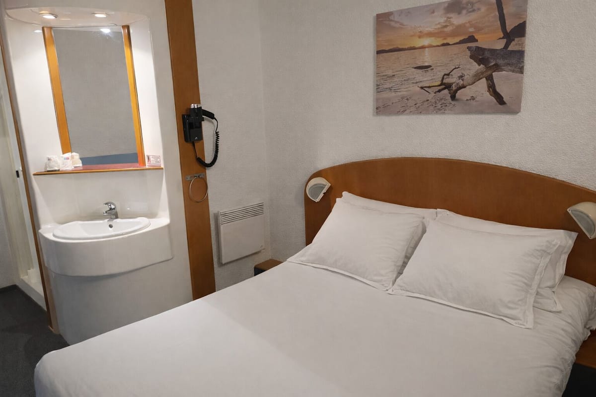 A hotel room with a bed, a white sink, and a mirror.