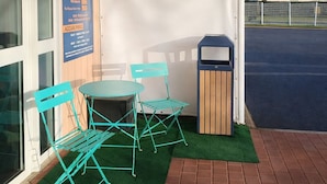 An outdoor seating area with a table and chairs, a trash bin, and a covered patio. - Quick Palace St Brieuc Tregueux (Tregueux)