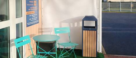 An outdoor seating area with a table and chairs, a trash bin, and a covered patio.