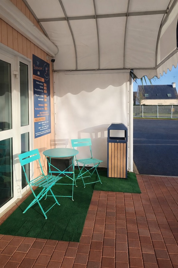 An outdoor seating area with a table and chairs, a trash bin, and a covered patio.