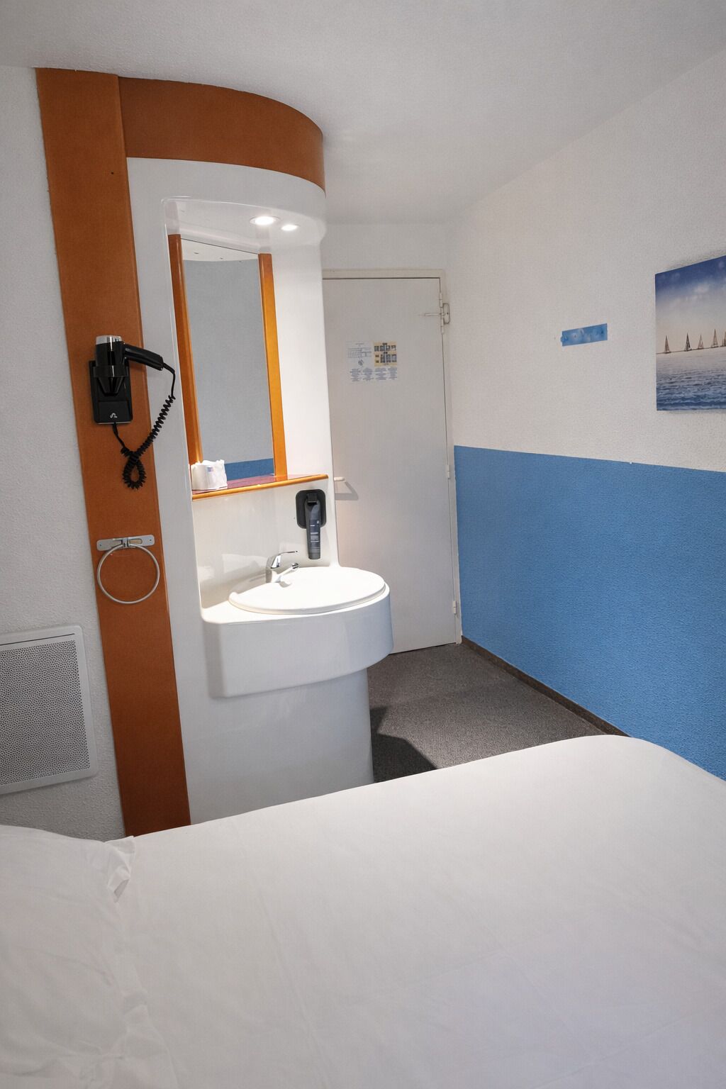 A hotel room with a white bed, a white sink, a telephone, and a mirror.