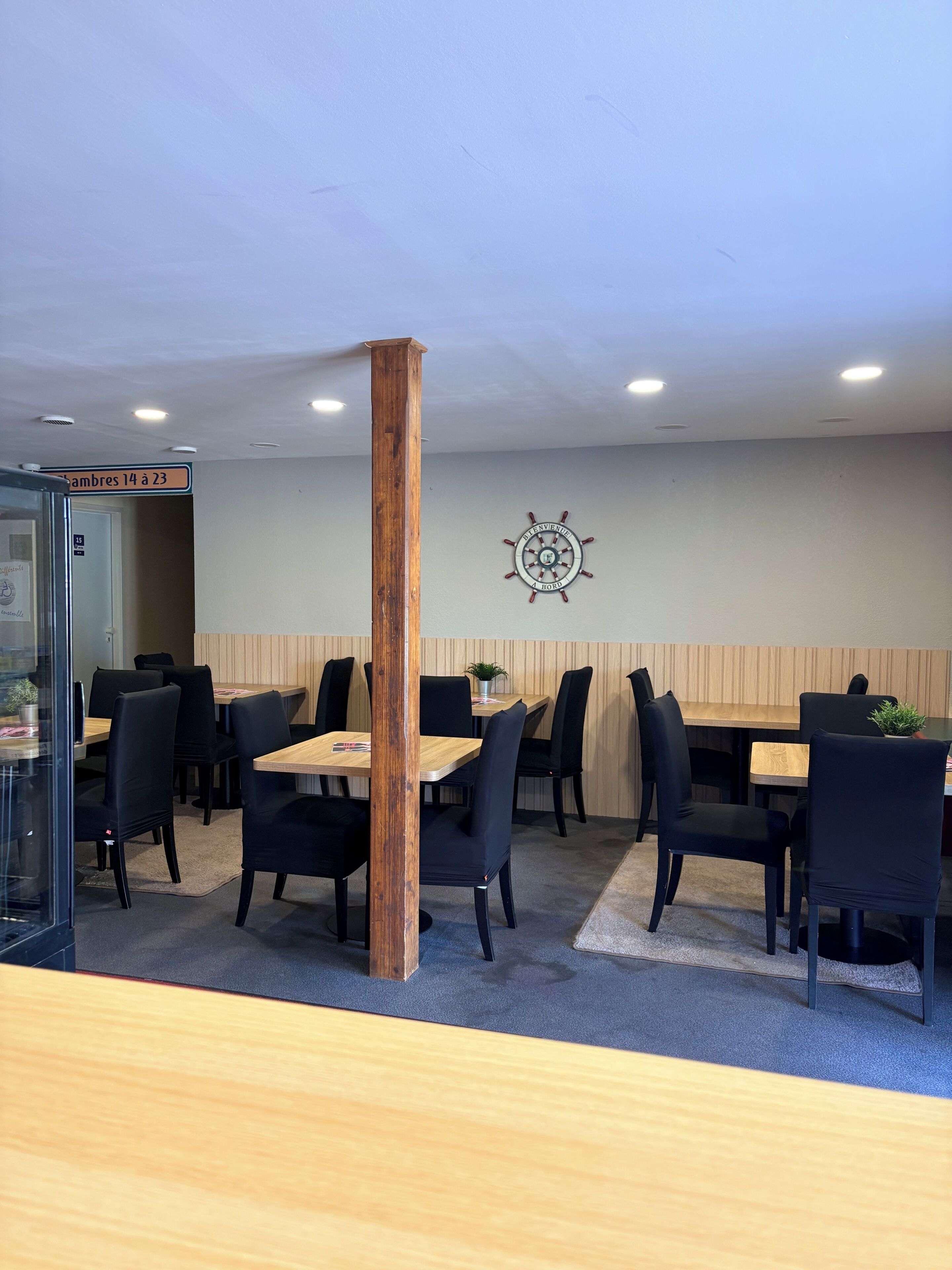En restaurang med träbord och svarta stolar, en träkolonn och en skeppsrat som dekoration på väggen.